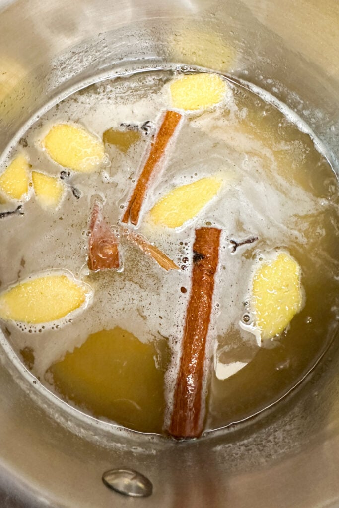 A pot of simmering non-alcoholic mulled wine with ginger slices, cinnamon sticks, and a few cloves visible.