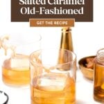 A glass of caramel old fashioned cocktail with ice, surrounded by caramel candies, syrup, a jigger, and another glass, rests invitingly on a white surface.