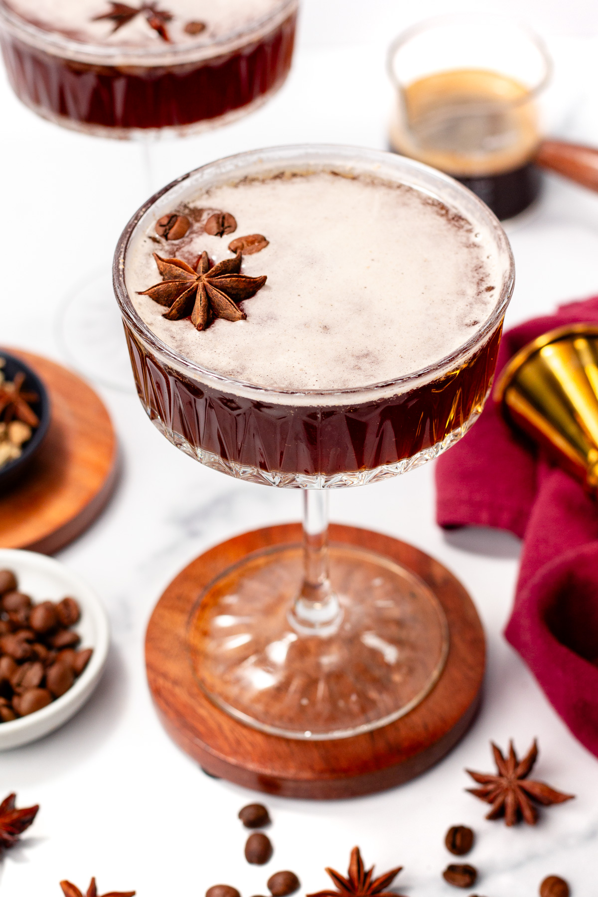 A cocktail served in a coupe glass, garnished with whole star anise, with coffee beans and cocktail tools in the background.