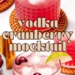A pink cranberry mocktail with ice, cranberries, and a lime wedge in a glass on a woven coaster, with the text "vodka cranberry mocktail" overlaid.