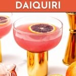 A glass of blood orange daiquiri garnished with a blood orange slice, set on a gold base, with bar tools and another drink in the background. Text reads "Blood Orange Daiquiri.