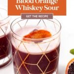 A glass of blood orange whiskey sour garnished with a blood orange slice, next to a partially visible glass and orange wedge, with recipe text above.