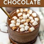A mug of hot chocolate topped with mini marshmallows and a straw, placed on a table, with text promoting an easy hot chocolate recipe from feastandwest.com.