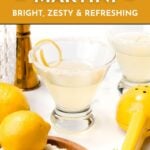 Two lemon drop martinis in sugar-rimmed glasses sit on a white surface with lemons, a lemon squeezer, and a cocktail shaker nearby. Text reads "Lemon Drop Martini - Bright, Zesty & Refreshing.