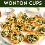 A plate of spinach and artichoke wonton cups is surrounded by small bowls of ingredients on a white surface, with a text overlay promoting the recipe.