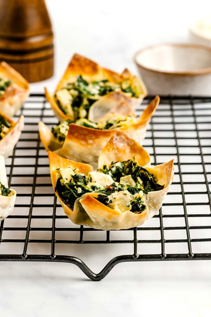 Spinach and cheese wonton cups cooling on a wire rack, with brown and white bowls in the background.