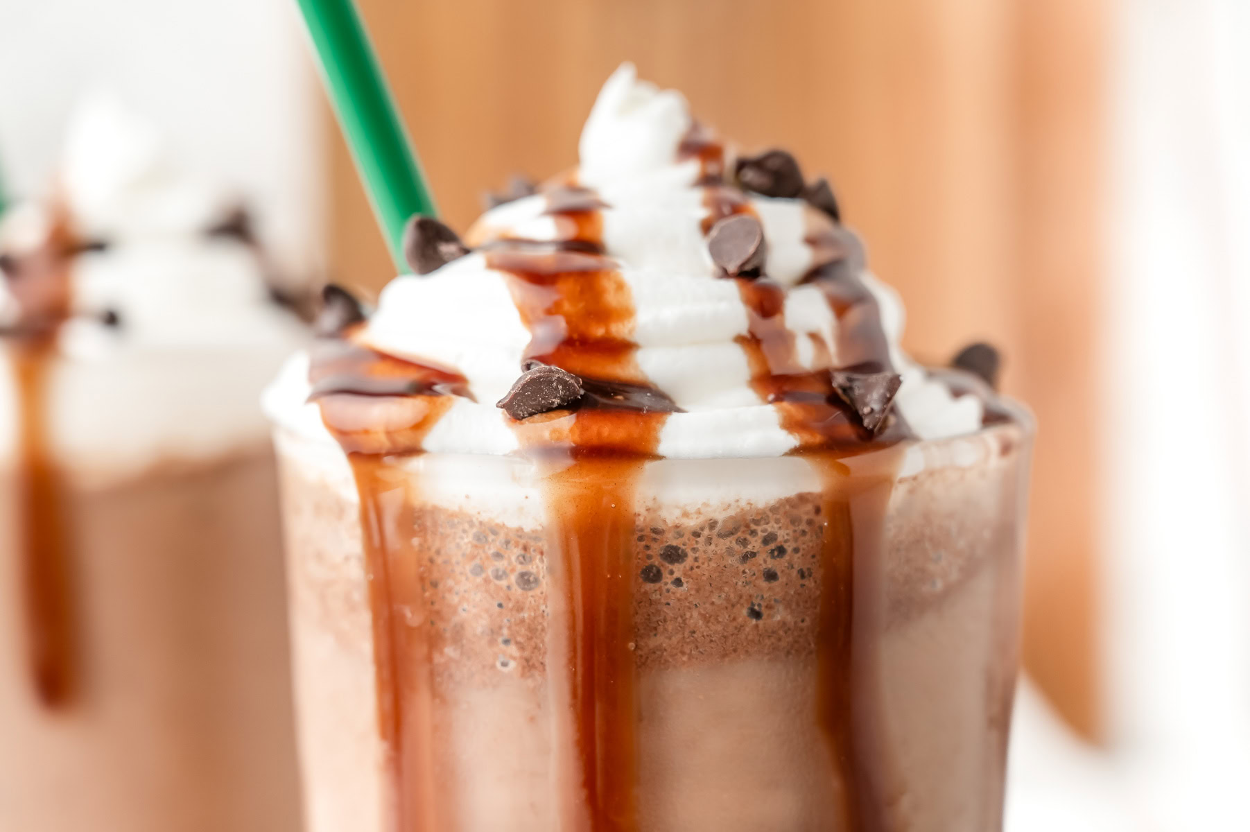 A blended chocolate drink topped with whipped cream, chocolate syrup, and chocolate chips, with a green straw.