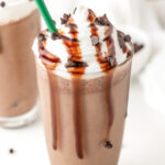 A glass of chocolate frappuccino topped with whipped cream, chocolate syrup, and chocolate chips, with a green straw.