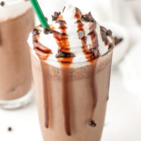 A glass of chocolate frappuccino topped with whipped cream, chocolate syrup, and chocolate chips, with a green straw.