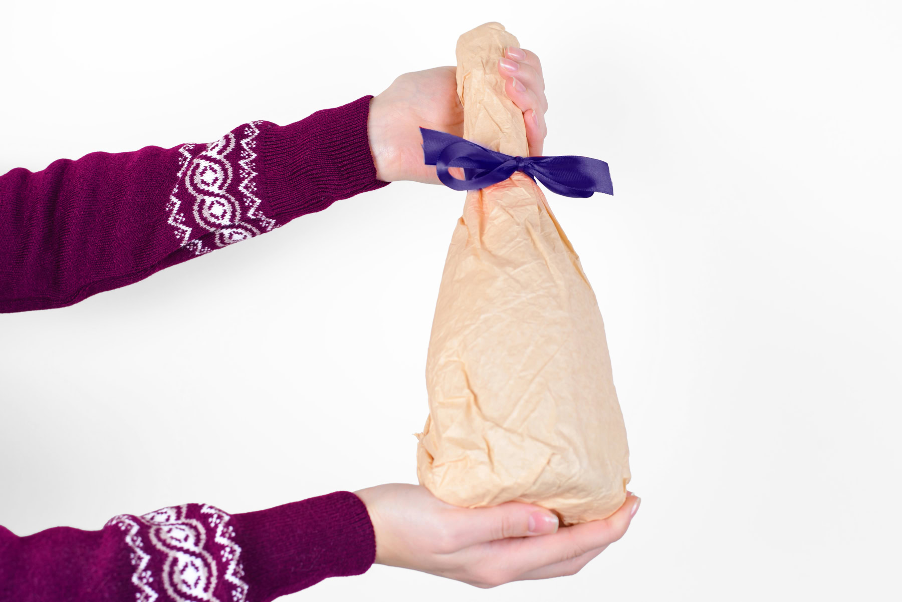A person in a purple sweater holds a beige, oddly shaped package tied with a dark blue ribbon against a plain white background.
