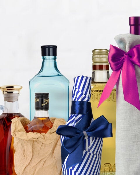 Five assorted liquor bottles, some wrapped in paper or fabric and some with bows, are arranged in a row against a plain white background.