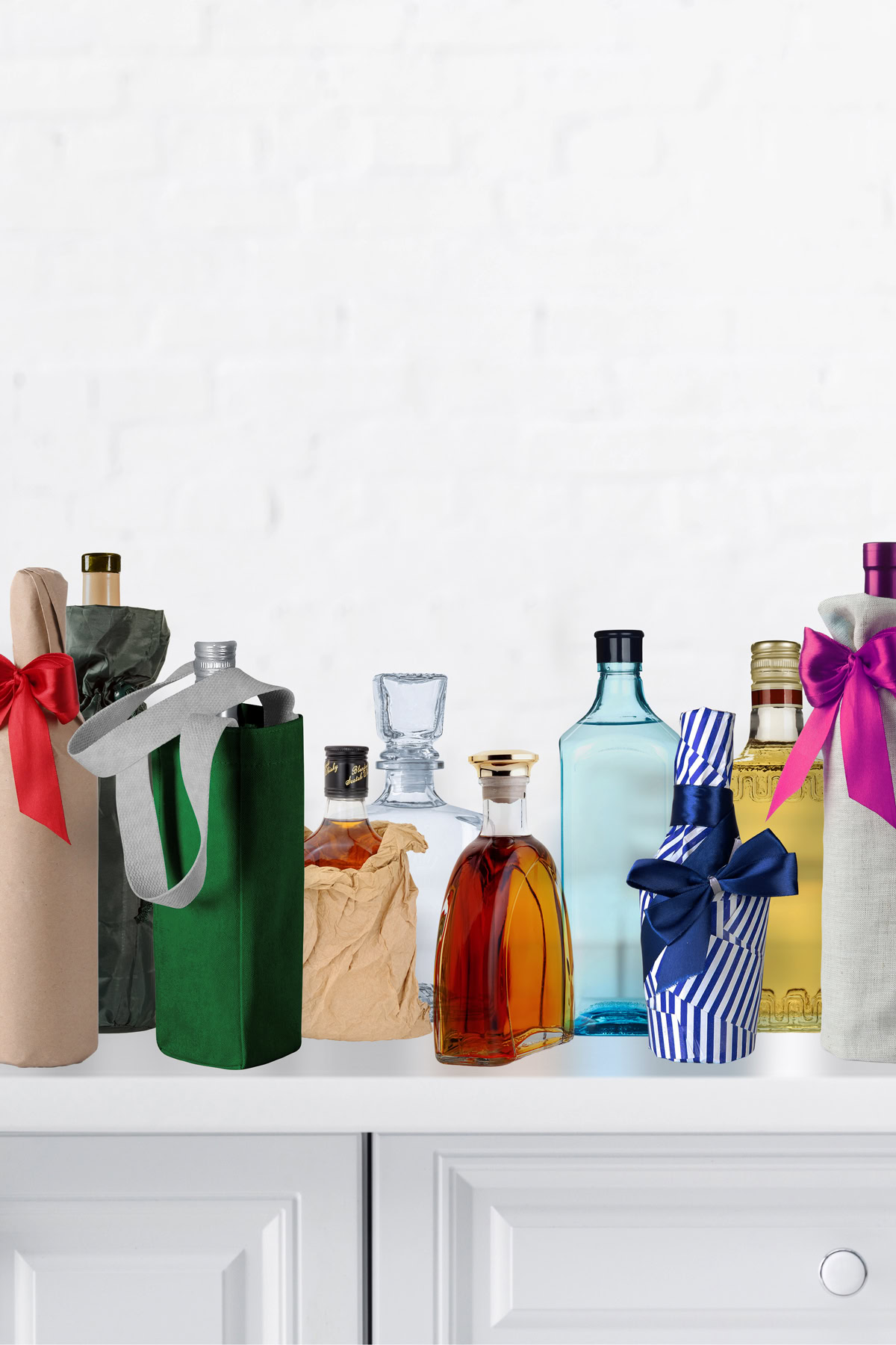 A variety of bottles, some wrapped in fabric or paper with ribbons, are arranged on a white countertop against a white background.