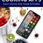 Smartphone displaying various cooking app icons surrounded by fruits, granola, and a marble cutting board. Text reads: "The Best Cooking Apps: Easy Hacks for Your Kitchen.