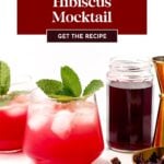 Two glasses of hibiscus mocktail with ice and mint garnish, a jar of hibiscus liquid, a jigger, and dried hibiscus petals on a white surface.