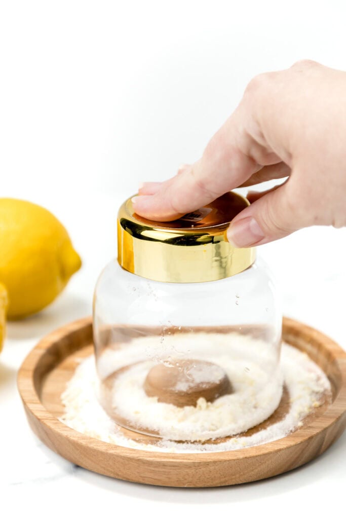 A hand presses a glass with a gold rim upside down into a plate of salt, with a lemon and a wooden plate nearby.