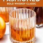 A glass of rye old fashioned sits on a white surface beside an orange, with text showcasing the recipe for this bold whiskey classic.
