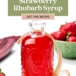 A bottle of strawberry rhubarb syrup sits in front of fresh strawberries and rhubarb, highlighting this easy homemade strawberry rhubarb syrup recipe.