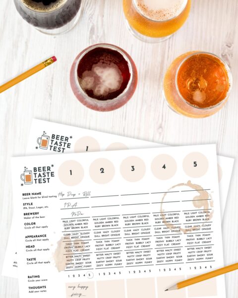Four glasses of beer and two beer tasting sheets with pencil and spilled beer on a white wooden table.