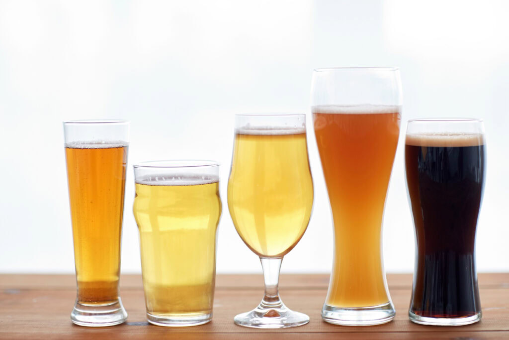 Five glasses of different types of beer in a row on a wooden surface, against a light background.