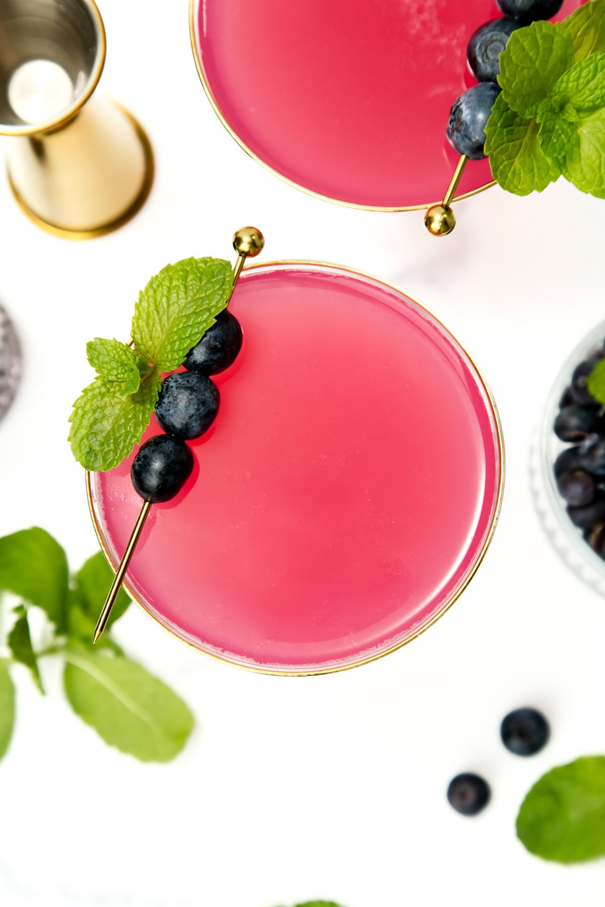 Pink cocktail in a glass, garnished with blueberries and mint on a skewer, viewed from above.