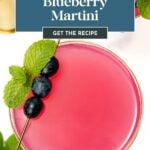 Bright pink blueberry martini garnished with blueberries and mint on a skewer, shown from above.