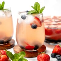 A glass of berry-infused iced drink with mint garnish, surrounded by fresh strawberries and blueberries.