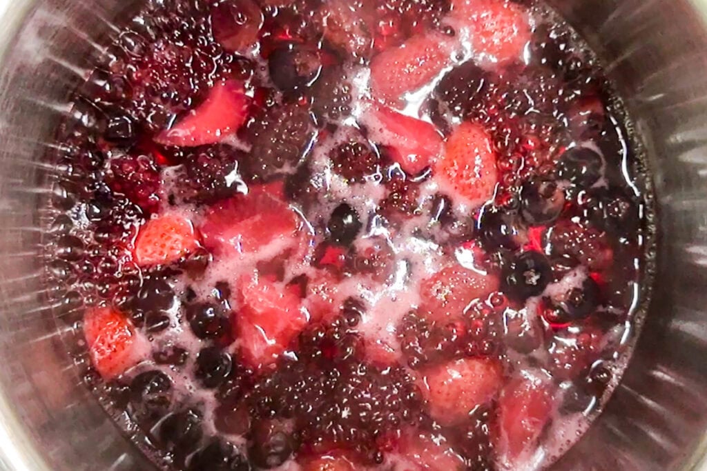 A pot of mixed berries simmering, including strawberries, blackberries, and blueberries in bubbling liquid.