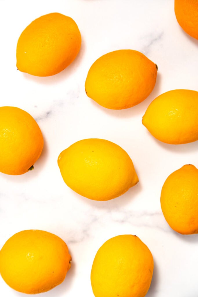 Several whole lemons are scattered on a white marble surface.