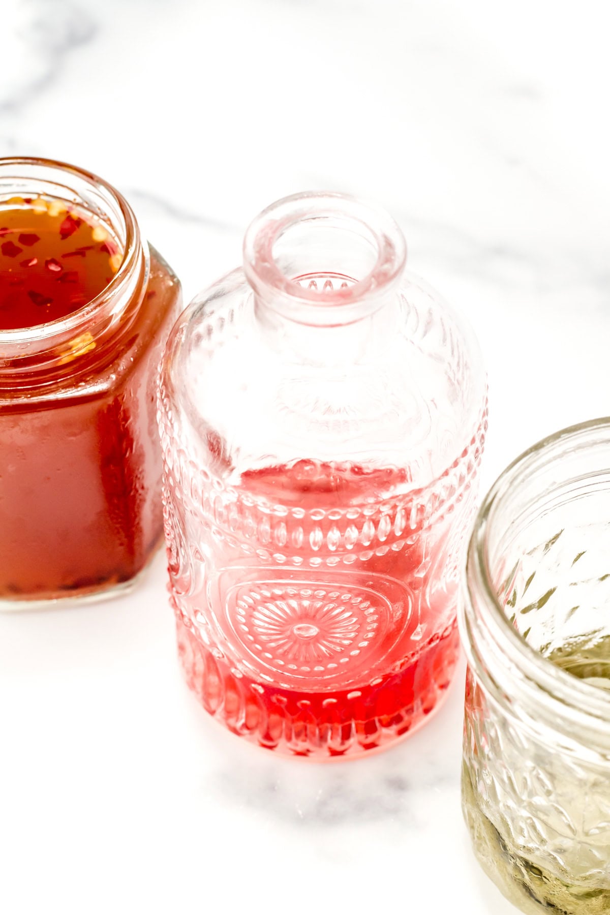 Three glass jars with different colored liquids—red, pink, and clear—on a white surface.