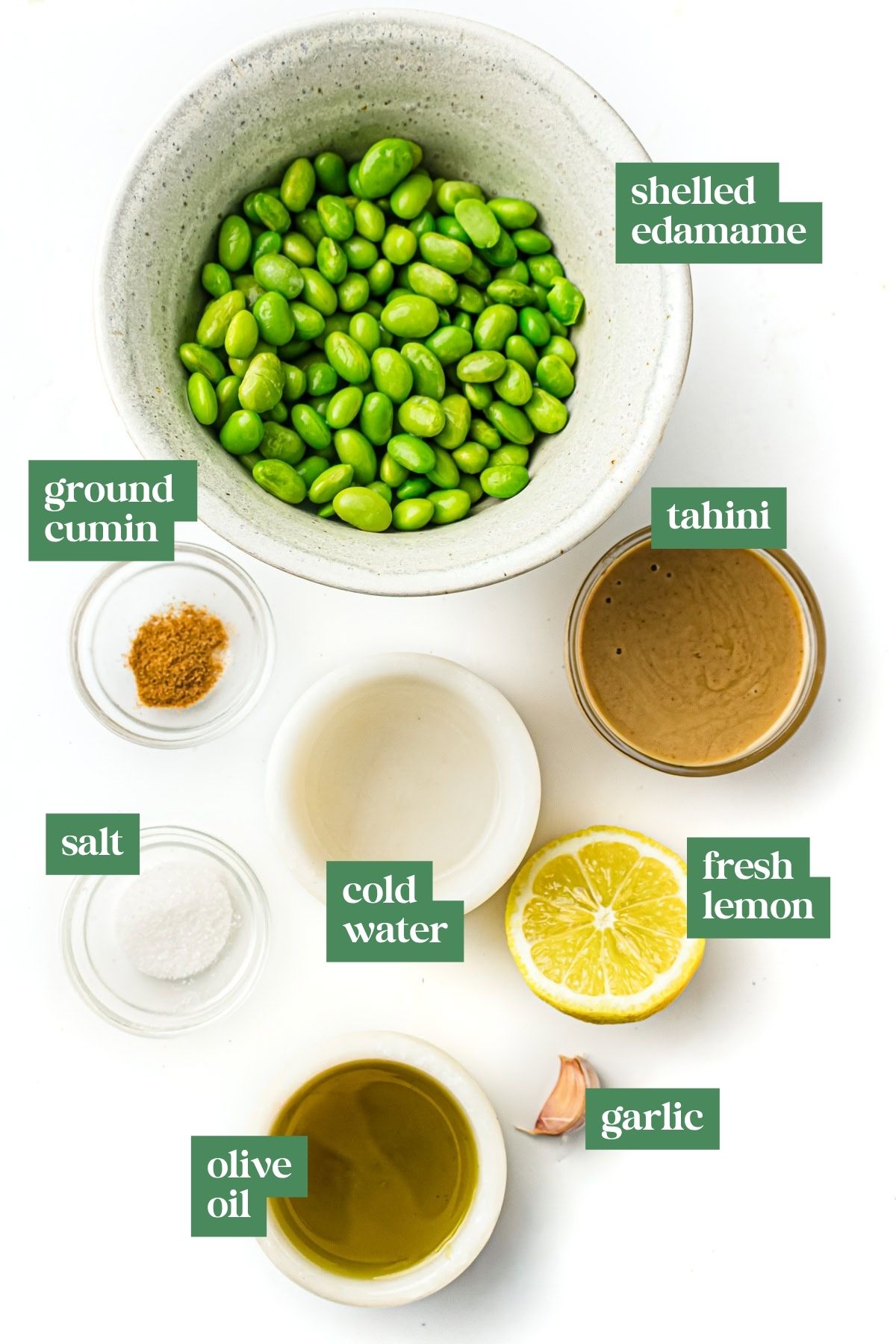 Ingredients for edamame hummus in bowls: edamame, tahini, cumin, salt, cold water, lemon, olive oil, and garlic.