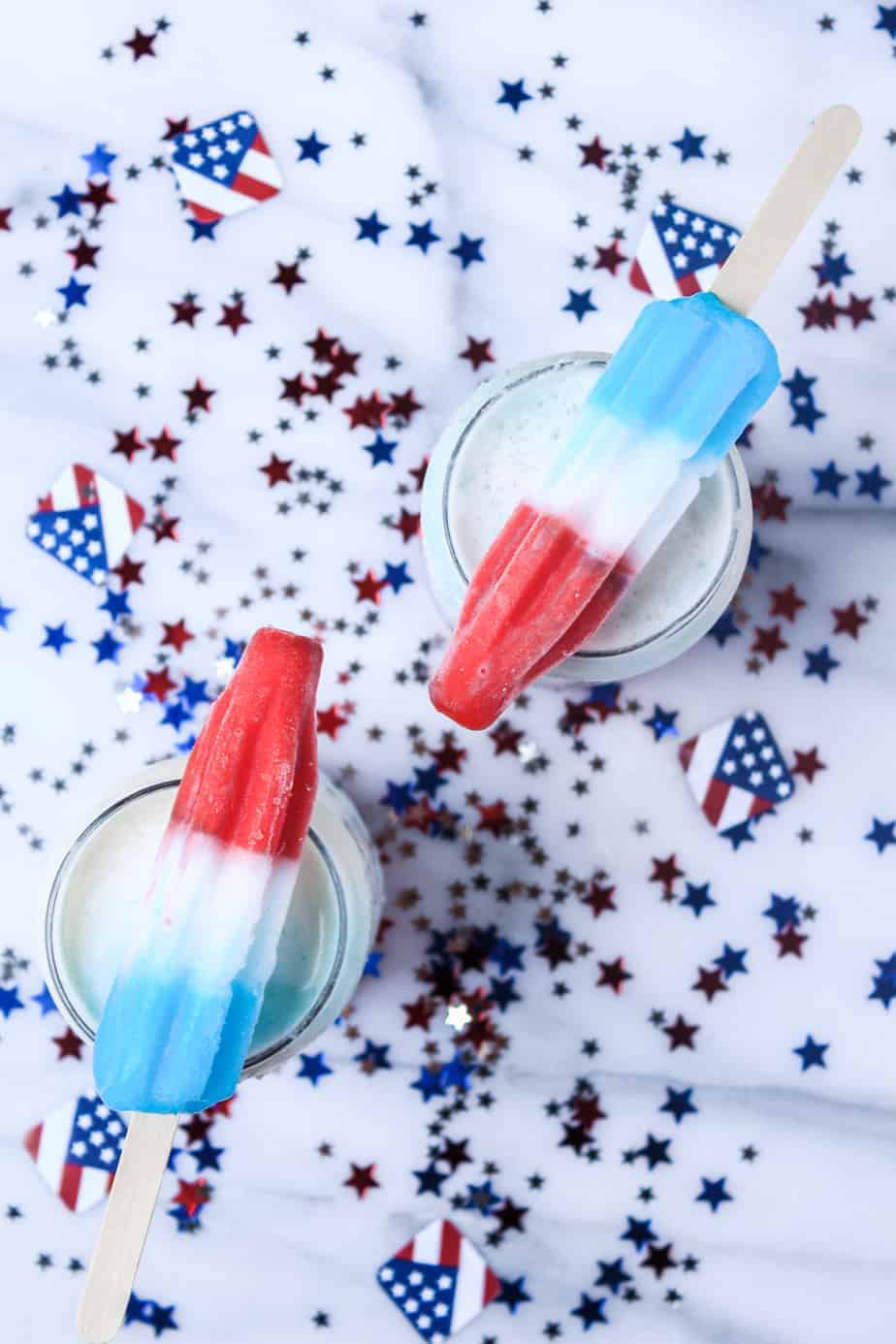 Red, white, and blue popsicles on drinks with star-shaped confetti and small American flag decorations.