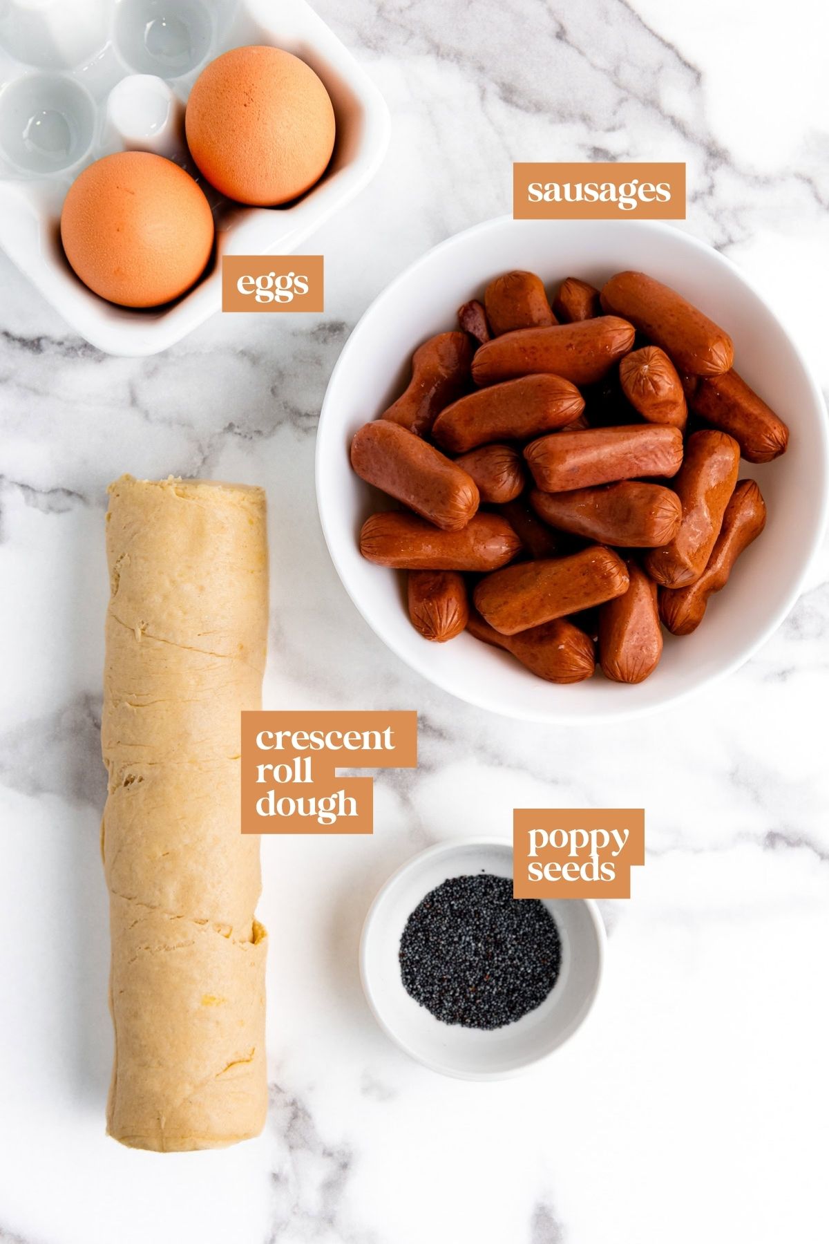 A marble counter with eggs, sausages, crescent roll dough, and poppy seeds labeled in bowls and dishes.