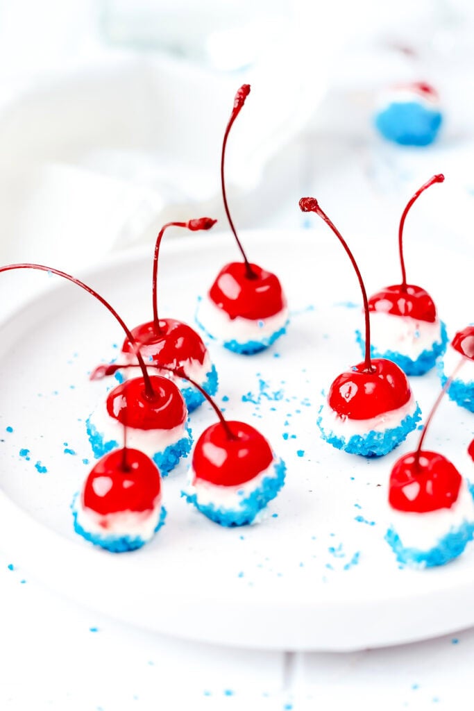 Maraschino cherries dipped in white and blue coatings, arranged on a white plate for a festive treat.