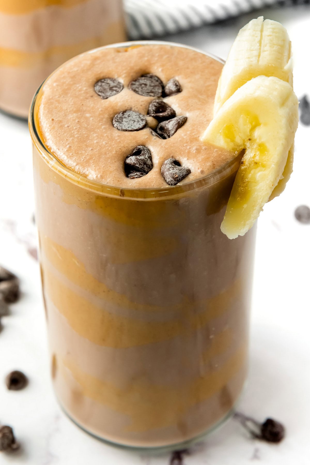 A glass of Chocolate Peanut Butter Power Smoothie topped with chocolate chips and banana slices on the rim.