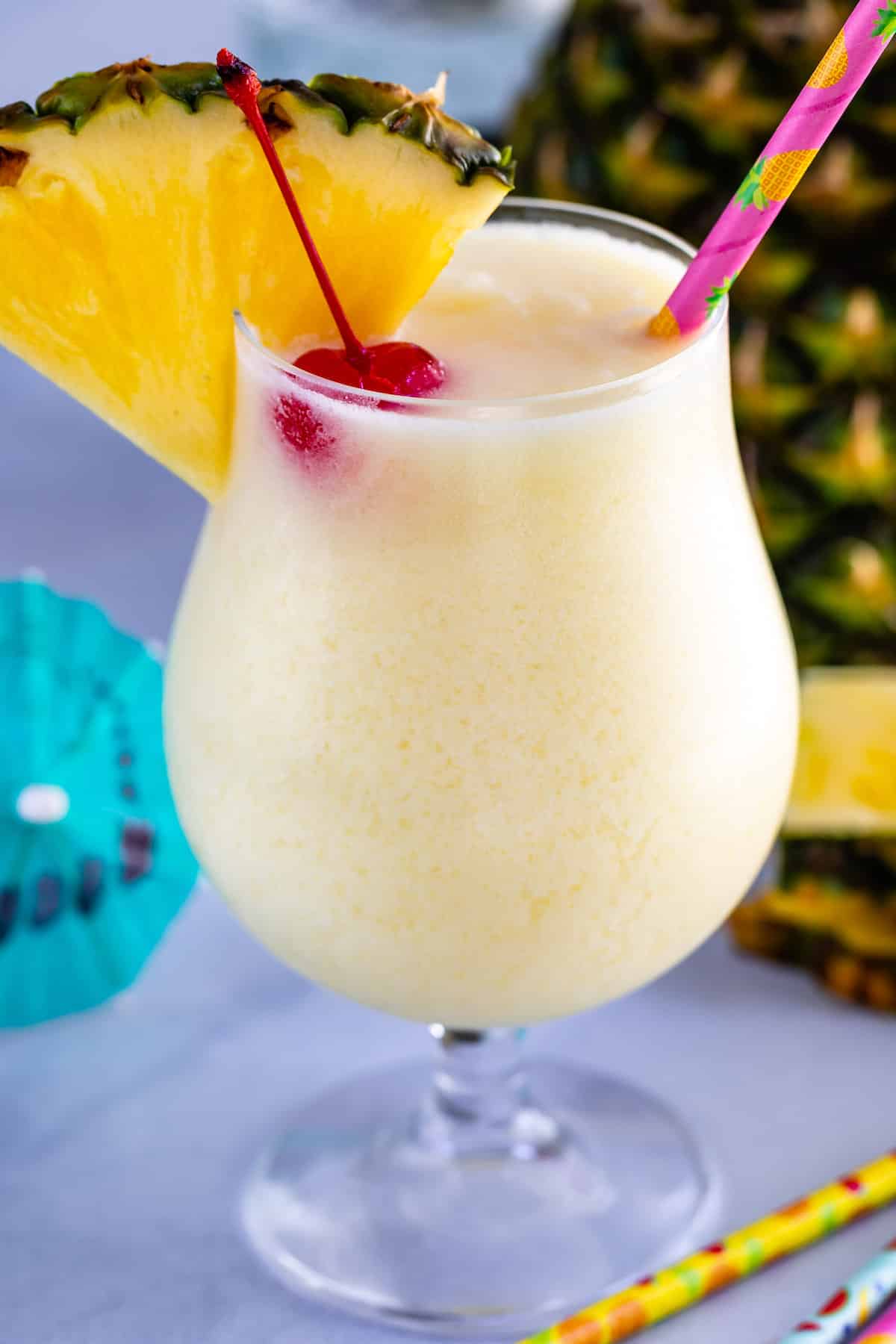 A pi&ntilde;a colada in a glass, garnished with a pineapple slice, cherry, and colorful straw&mdash;one of the best summer beverages and perfect for those wondering what to drink in July.