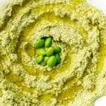 Green hummus topped with whole edamame beans, served in a white bowl.
