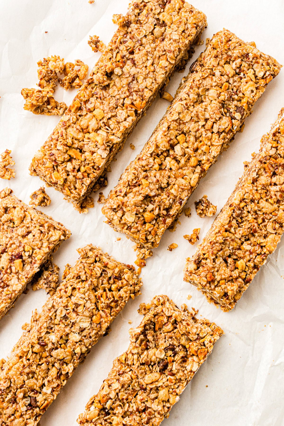 Six homemade granola bars arranged on parchment paper, with visible oats and nuts.