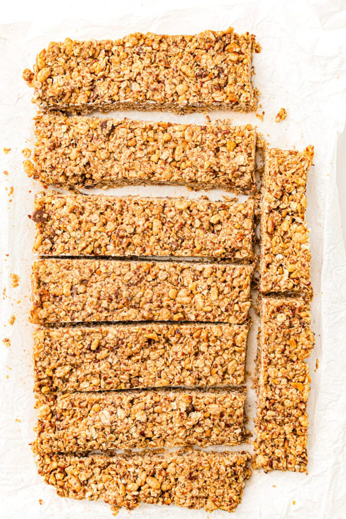 Eight rectangular granola bars on parchment paper, arranged neatly with a few crumbs around them.