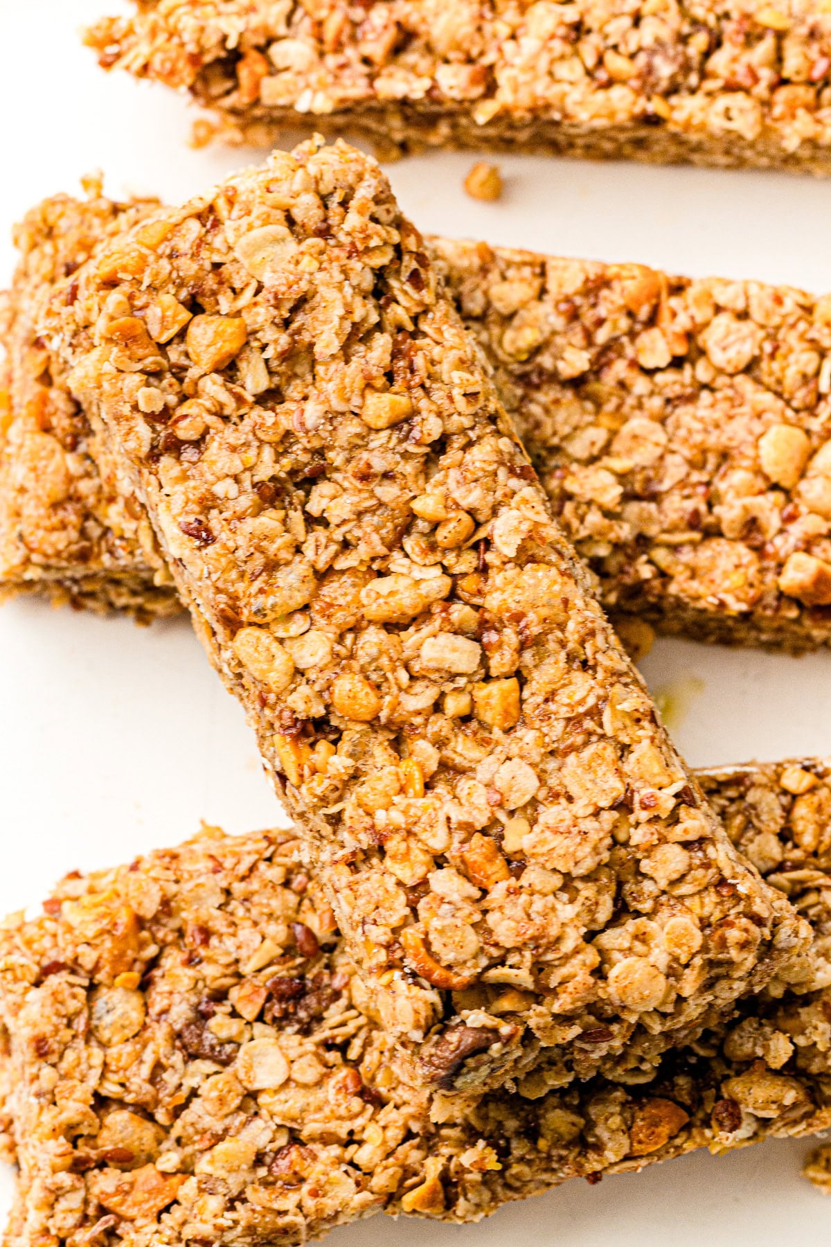 Four granola bars stacked on a white surface, showing their oat and nut texture up close.