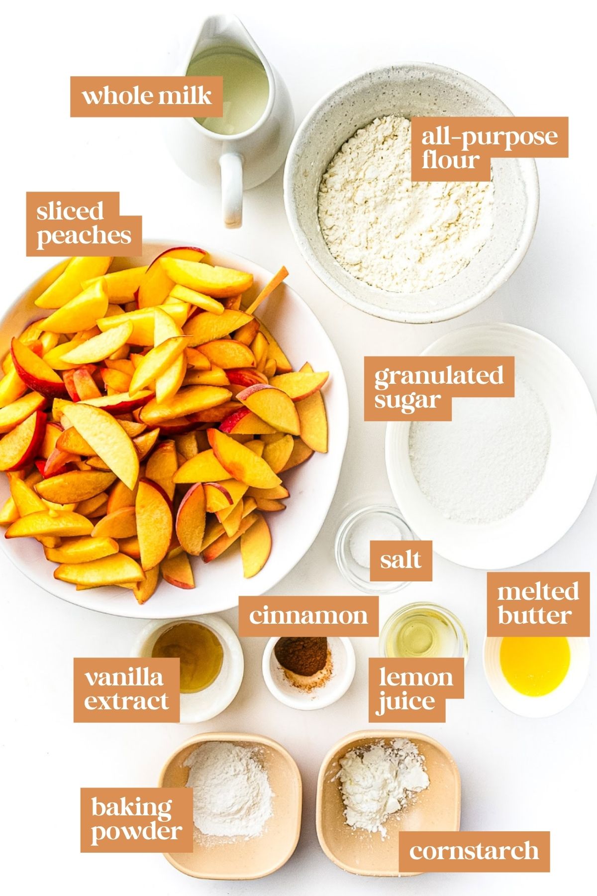 Sliced peaches and labeled bowls of flour, sugar, milk, and other baking ingredients on a white surface.