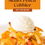 A serving of skillet peach cobbler topped with vanilla ice cream on a white plate.