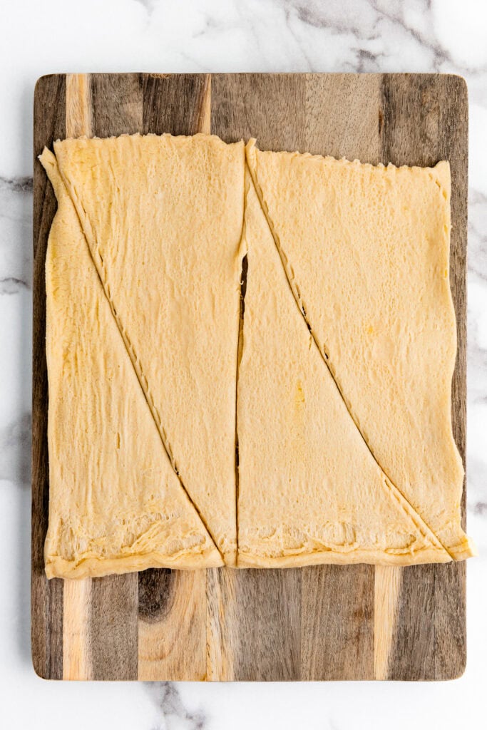 Rectangular dough sheet on a wooden board, cut diagonally into two large triangles.