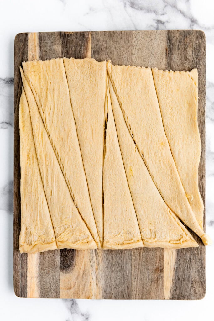 Unbaked crescent roll dough cut into triangles on a wooden cutting board.