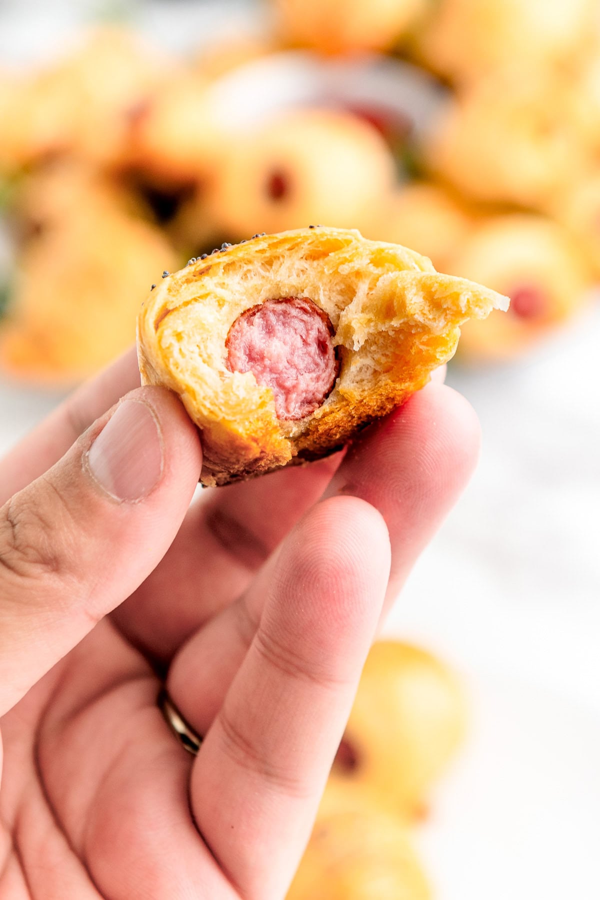 A hand holding a bitten mini sausage wrapped in golden, flaky pastry.