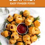 A plate of pigs in a blanket with a bowl of ketchup in the center, garnished with rosemary sprigs.
