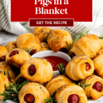 A plate of pigs in a blanket with poppy seeds, garnished with rosemary, and a dish of ketchup.