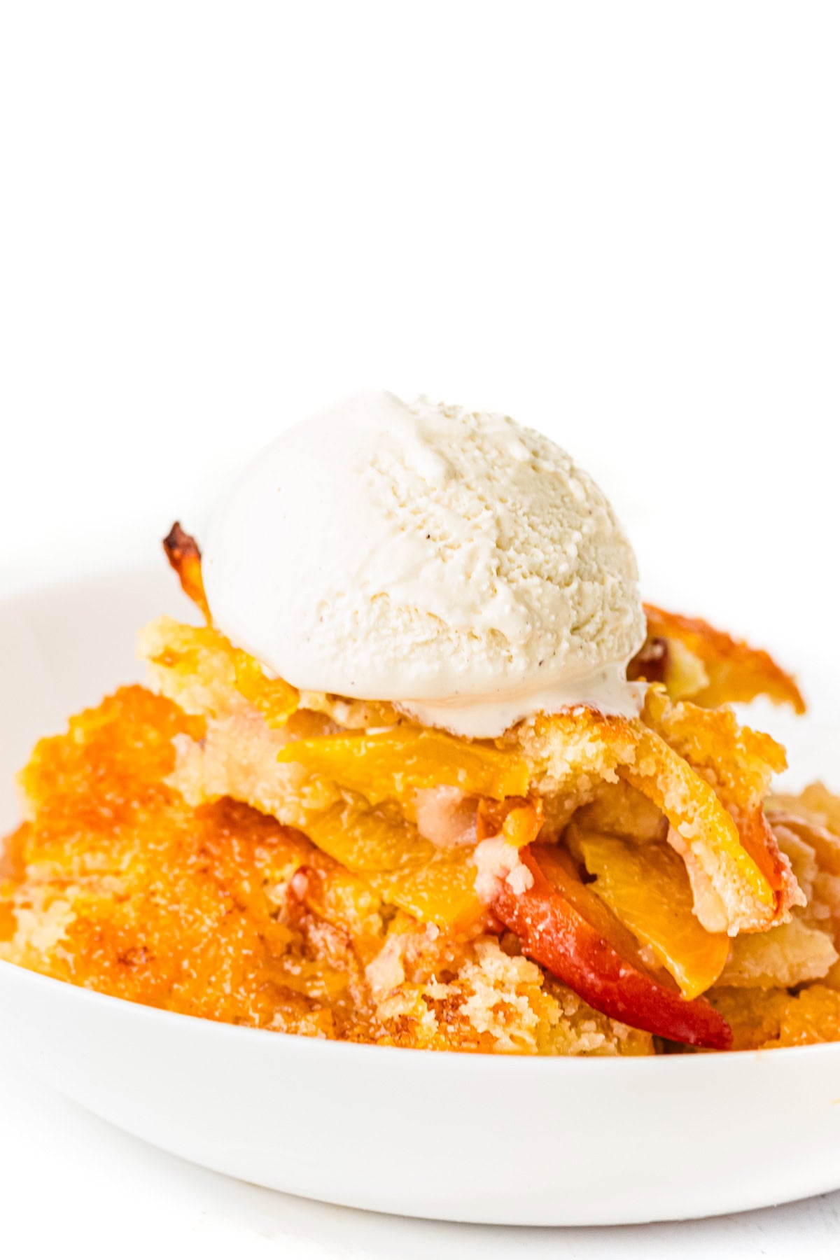 A serving of peach cobbler topped with a scoop of vanilla ice cream on a white plate.
