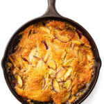 Golden-brown fruit cobbler with sliced peaches baked in a cast iron skillet, viewed from above.