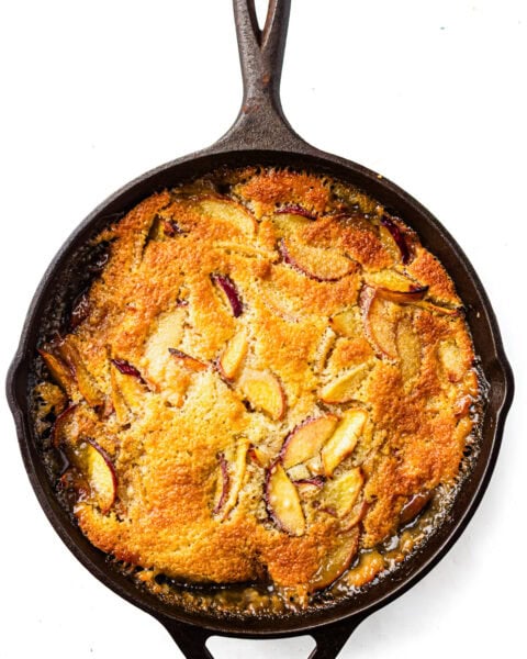 Golden-brown fruit cobbler with sliced peaches baked in a cast iron skillet, viewed from above.