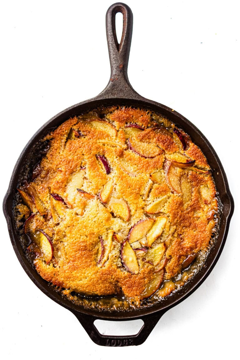 Golden-brown fruit cobbler with sliced peaches baked in a cast iron skillet, viewed from above.